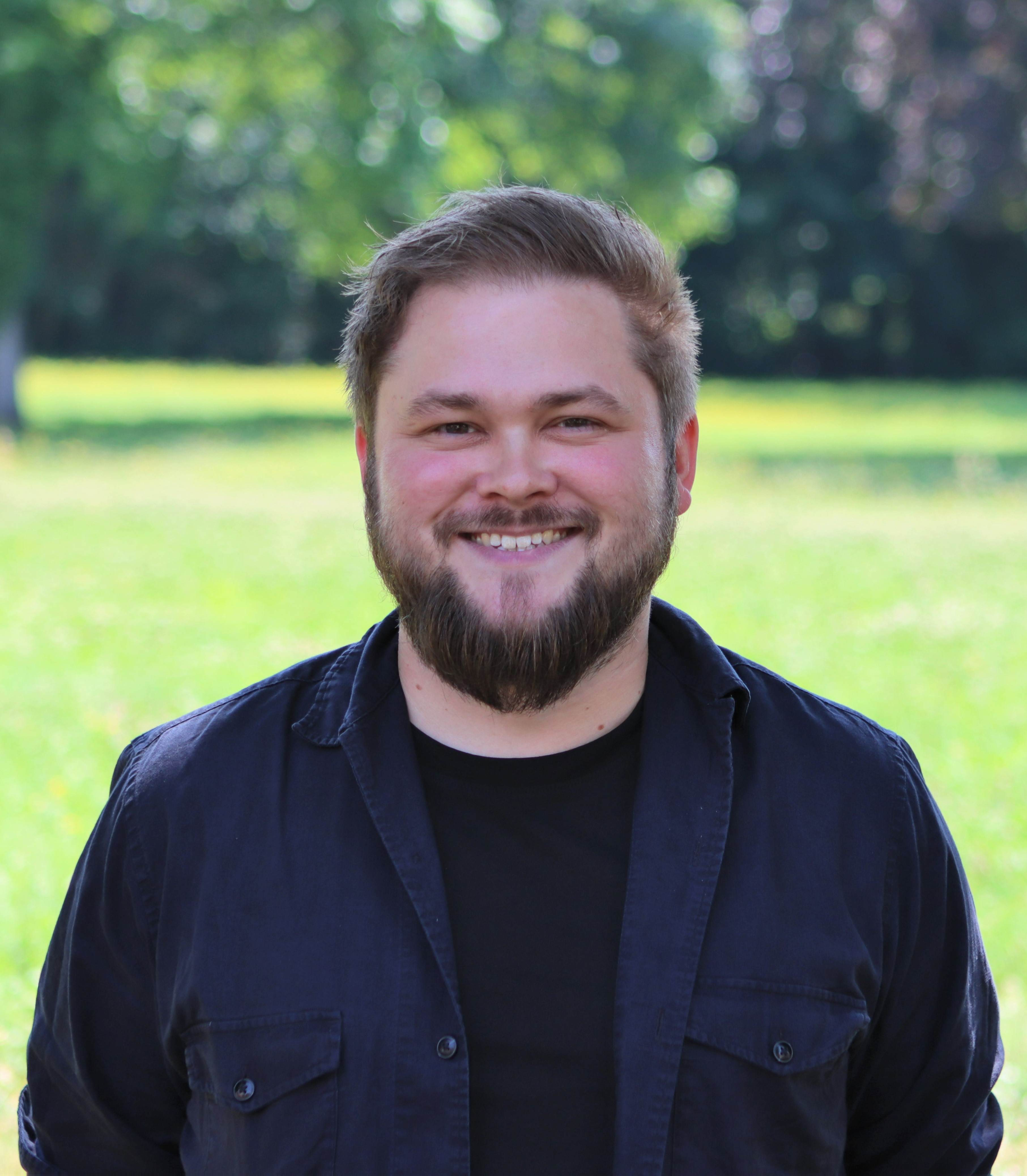 Daniel Schilling lächelt in die Kamera, im Hintergrund grüne Wiese und Bäume