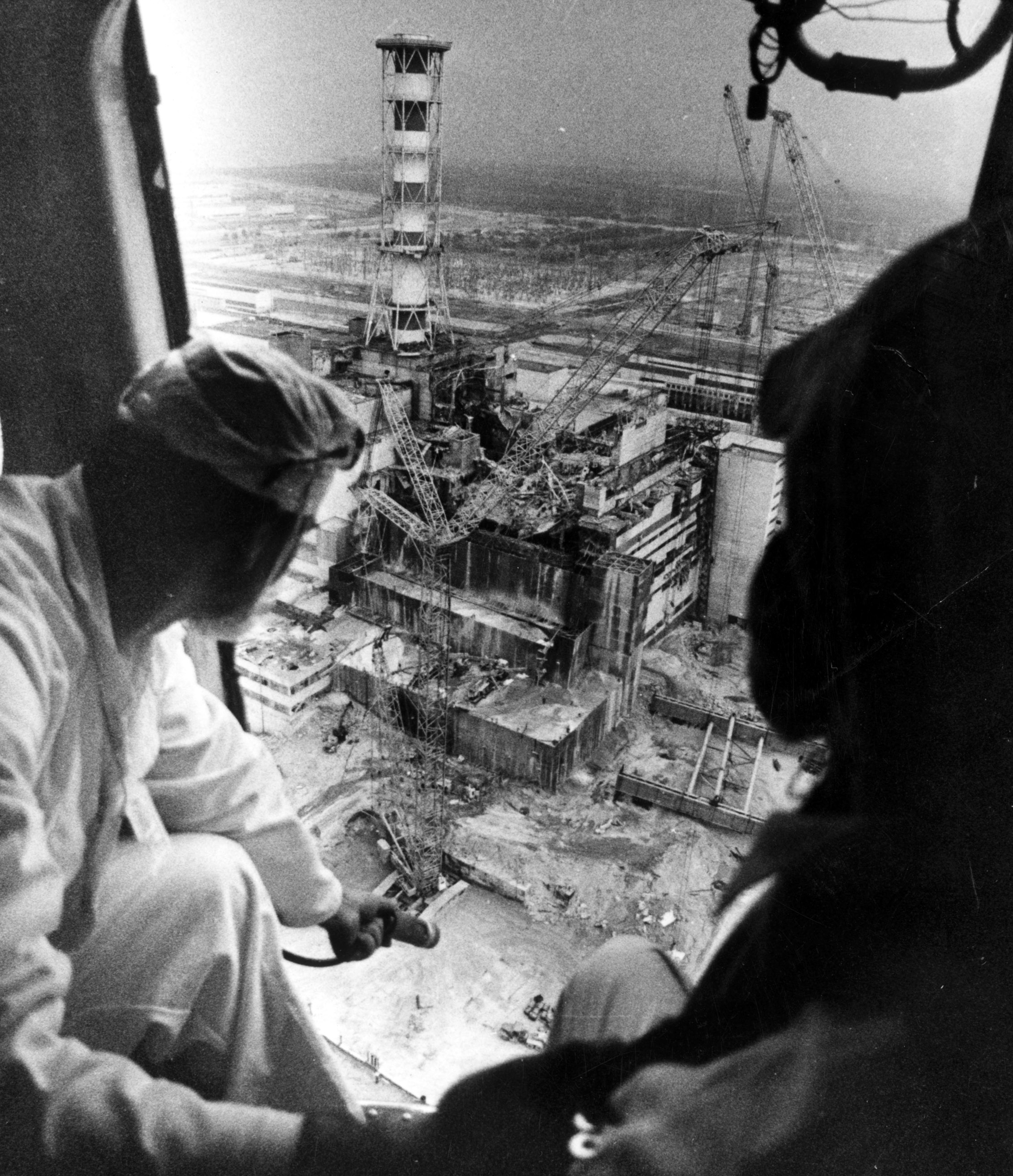 Zwei Menschen halten ein Messgerät aus einem Helikopter über dem zerstörten Reaktor von Tschernobyl.