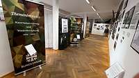 Blick in einen Ausstellungsbereich mit Aufstellern und Bildern an der Wand