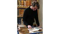 Ein Projekt-Mitarbeiter steht vor einem Bücherregal und überprüft ein Buch auf Provenienzspuren.