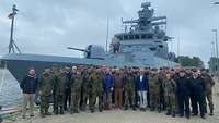 Eine 40-köpfige Besuchsgruppe lässt sich vor einem Schiff der Marine fotografieren.