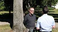 Alaric Searle und Michael Gutzeit im Gespräch vor Baumstamm
