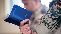 Hand eines Soldaten hält ein blaues Gebetsbuch mit dem Titel Lebensrhythmen