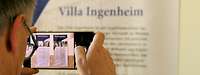 Hinterkopfansicht eines Mannes wie er mit dem Handy Plakate der Villa Ingenheim fotografiert