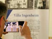 Villa Ingenheim mit Blick durchs Handy Hinterkopfansicht eines Mannes wie er mit dem Handy Plakate der Villa Ingenheim fotografiert