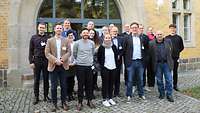 17 Personen stehen aufgestellt für das Gruppenbild und schauen freundlich in die Kamera