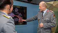 Eine Soldatin interviewt einen Soldaten im Studio. Der Soldat erkärt etwas an einem Monitor.
