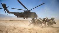 Soldaten schützen sich vor einem startenden Hubschrauber vor aufgewirbeltem Sand.