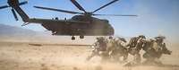 Soldaten schützen sich vor einem startenden Hubschrauber vor aufgewirbeltem Sand.