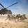 Soldaten schützen sich vor einem startenden Hubschrauber vor aufgewirbeltem Sand.