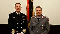 Zwei Stabsoffiziere in schwedische Marine- und deutscher Heeresuniform vor deutscher Truppenfahne der Bundeswehr.