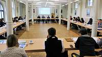 ca. 30 Personen sitzen im Saal bei einer Besprechung zusammen