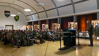 Ein Offizier trägt in einem Saal vor 50 sitzenden Personen vor.