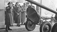 Mehrere Personen in militärischen Uniformen betrachten ein Artilleriegeschütz.