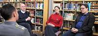 Gruppe aus zwei Wissenschaftlern und einer Wissenschaftlerin im Interview mit Offizier sitzend.