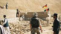 Bundeswehrsoldaten und zivile Afghanen stehen auf einer Baustelle, Maueransätze sind schon gebaut.