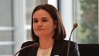 Portraitfoto der Oppositionspolitikerin Swjatlana Tsichanouskaja an einem Tisch hinter Mikrofonen