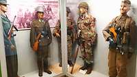 5 Puppen in einer Vitrine mit unterschiedlichen Waffen und Uniformen