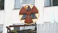 Dreiflügliges Symbol für Radioaktivität in einem Kris vor einer Hauswand.