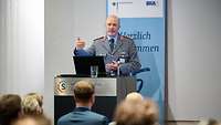 Foto eines Mannes in Uniform, der vor Publikum einen Vortrag hält