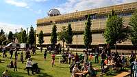 Festwiese mit Besuchergruppen, spielenden Kindern und Sitzgeelgenheiten