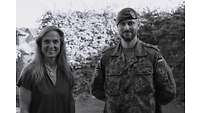 Eine Frau und ein Mann in Uniform vor einer Hecke