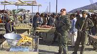 Ein Bundeswehrsoldat steht vor einem Marktstand, im Hintergrund zahlreiche Menschen.